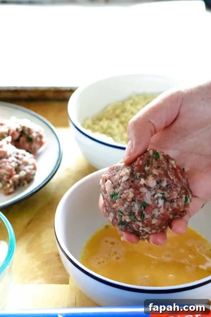 egg wrapped in meat being dipped into beaten egg