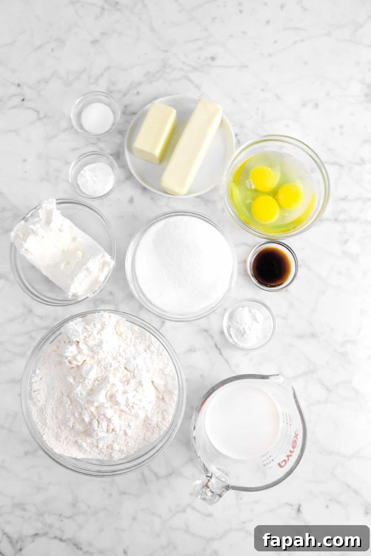 salt, baking powder, baking soda, butter, sugar, eggs, vanilla, cream cheese flour, and milk on marble counter