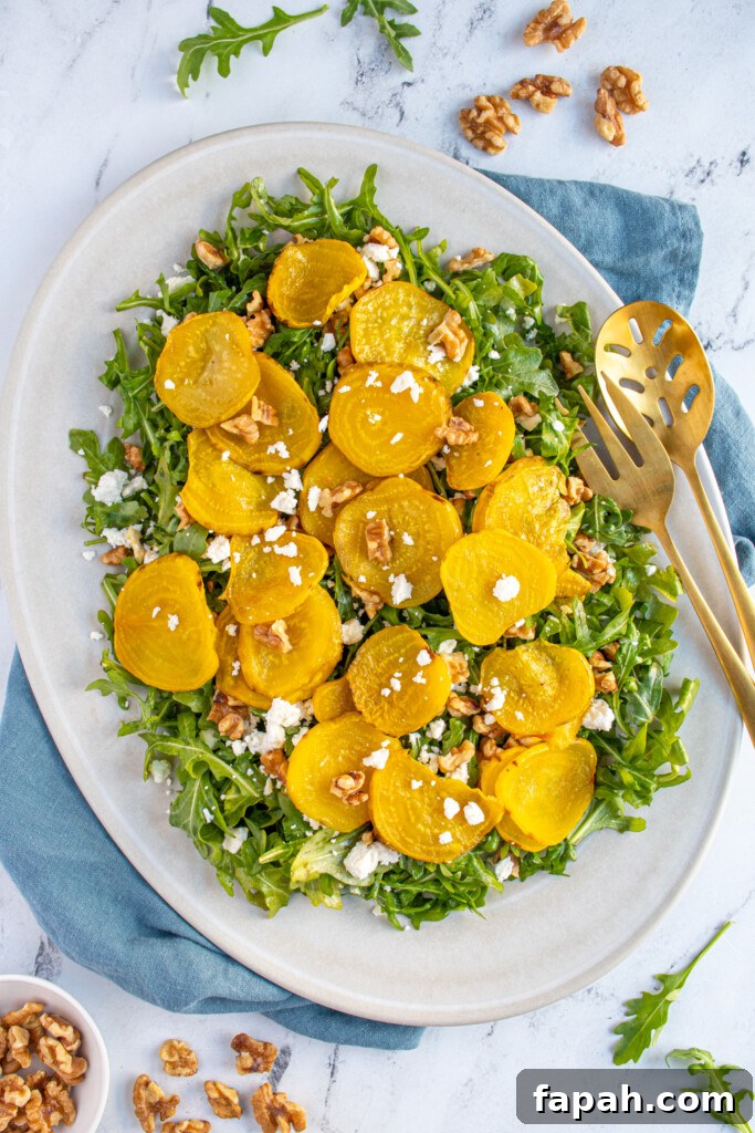 Arugula & Roasted Golden Beet Salad with Citrus Vinaigrette 3 Overhead view of a white platter filled with arugula and topped with roasted golden beets, walnuts, and feta cheese.