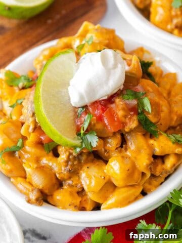 Small white bowl filled with taco mac and cheese, garnished with sour cream, salsa, chopped cilantro, and a lime slice.