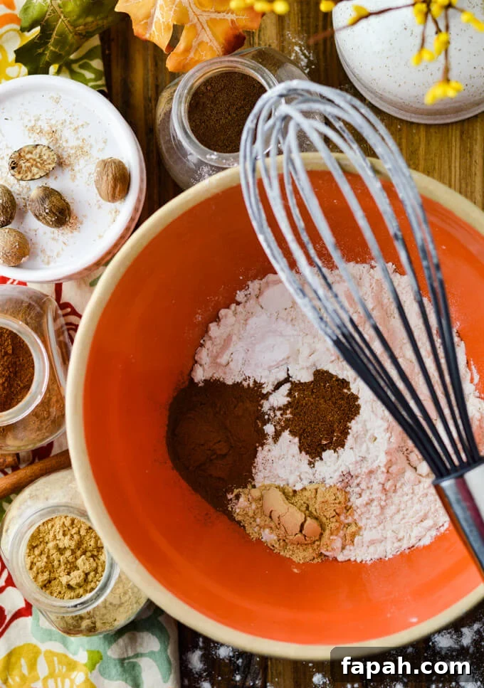Salted Caramel Pumpkin Cake Roll Recipe for Fall Desserts 3 Flour and spices in an orange mixing bowl with a whisk sitting on the bowl. jars of spices sit around the bowl.