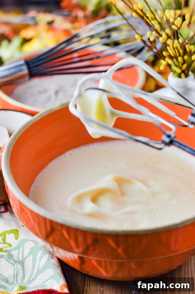 Salted Caramel Pumpkin Cake Roll Recipe for Fall Desserts 4 An orange mixing bowl of beaten eggs with hand mixing beaters above the bowl.