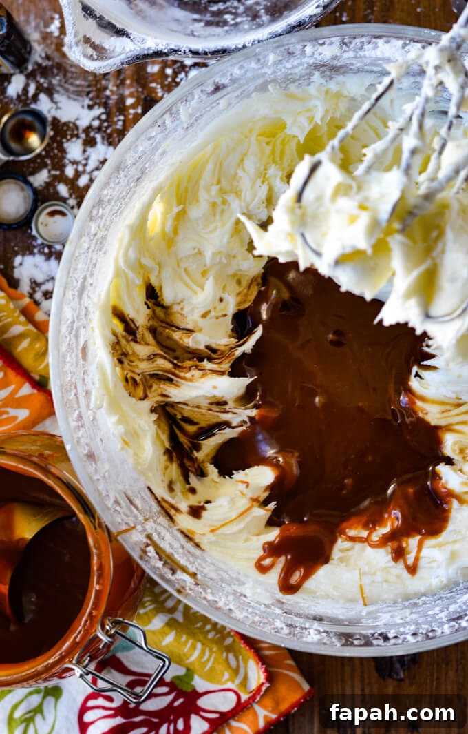 Salted Caramel Pumpkin Cake Roll Recipe for Fall Desserts 10 A bowl of mixed cream cheese icing with salted caramel dumped into it. Beaters rest above the bowl. A jar of salted caramel sauce sits on a colorful napkin and sits next to the bowl.