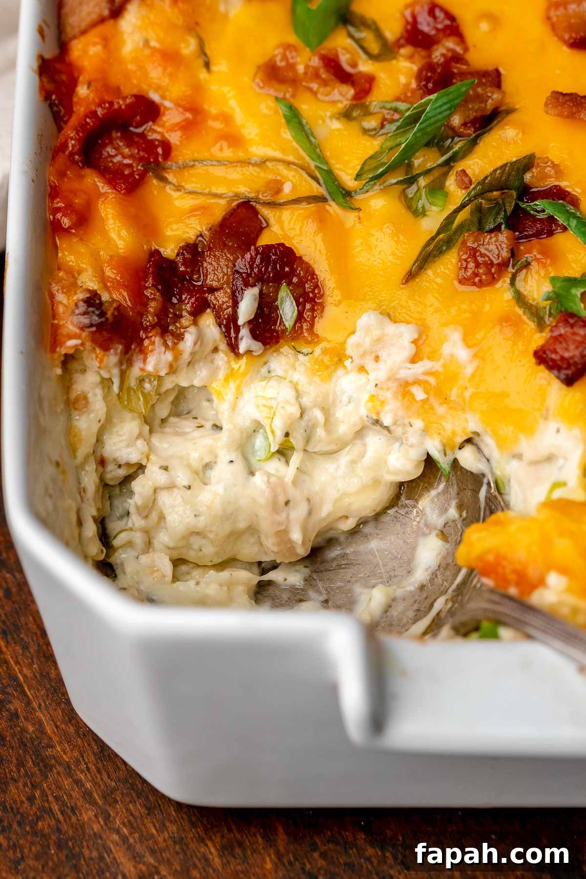 Cheesy Chicken Bacon Ranch Dip — Oven or Crockpot Recipe 2 A spoon scoops out a spoonful of chicken bacon ranch dip from the corner of a casserole dish.