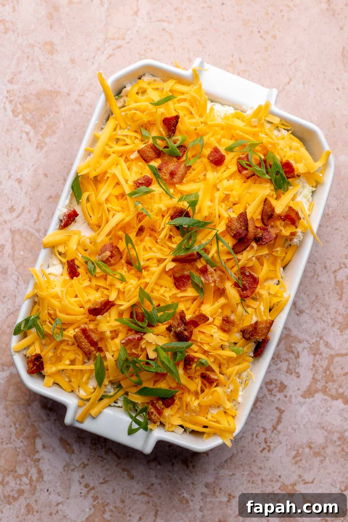 Cheesy Chicken Bacon Ranch Dip — Oven or Crockpot Recipe 7 Chicken bacon ranch dip covered in cheese, bacon, and scallions in a casserole dish before baking.