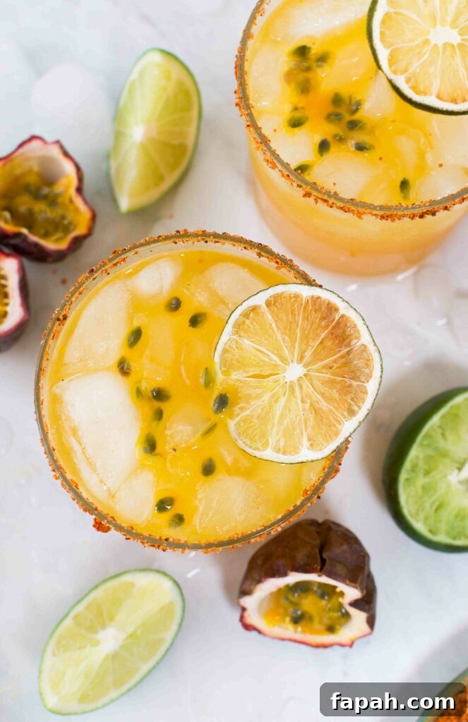 Overhead of two passion fruit margaritas surrounded by ice, passion fruits and limes