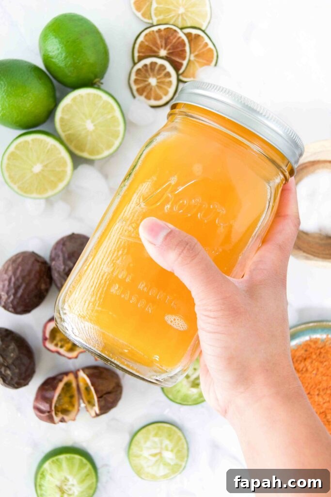 A orange mixed drink in a mason jar is shaken by a hand