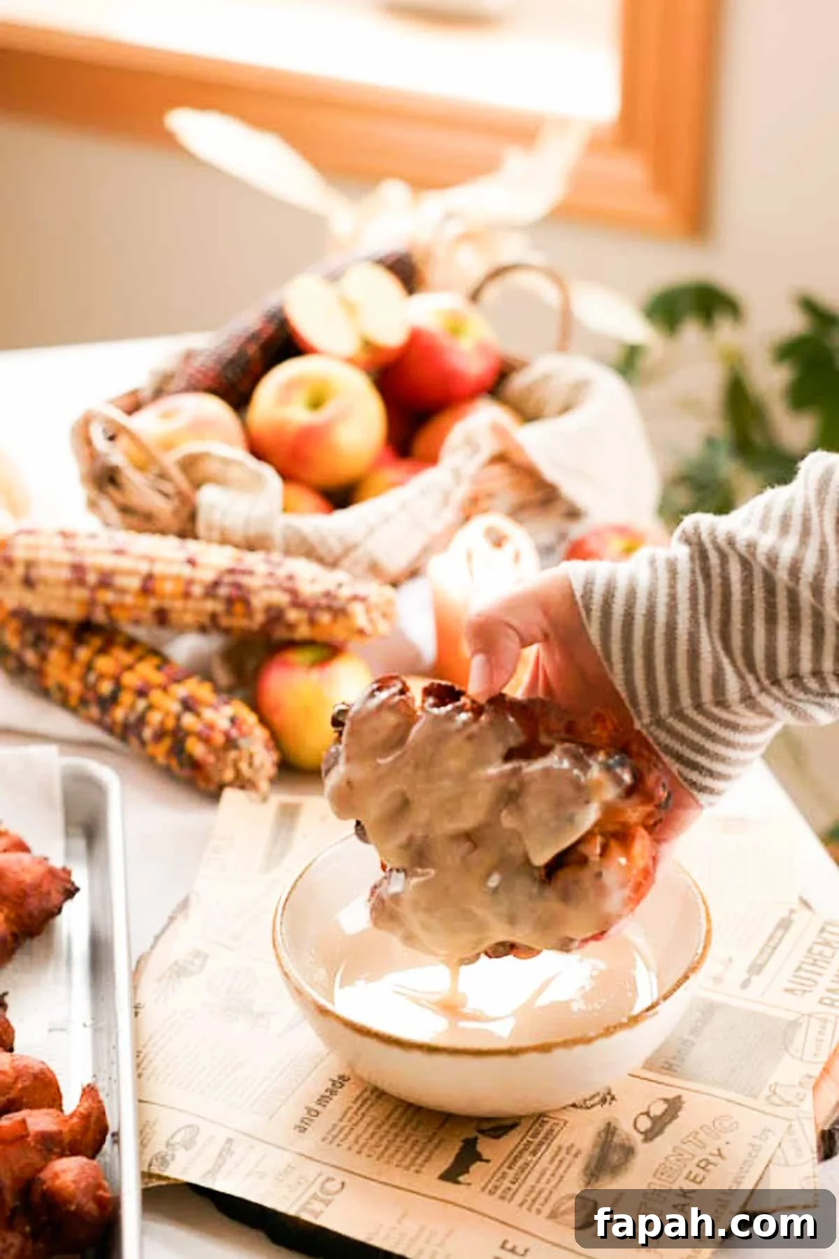 dipping apple fritters into a bowl with glaze