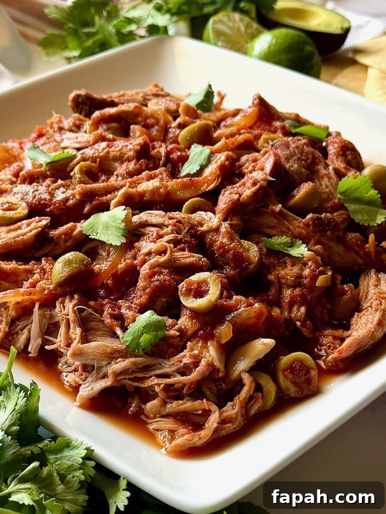 Slow cooker Spanish pulled pork on a serving plate with green olives and cilantro.