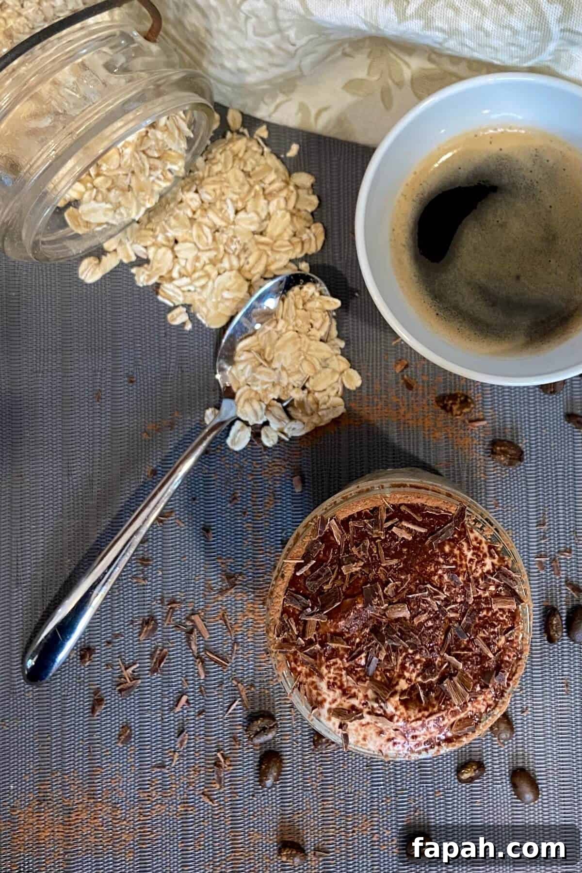 A jar of oats spilled onto a table with a cup of coffee and the overnight oats.