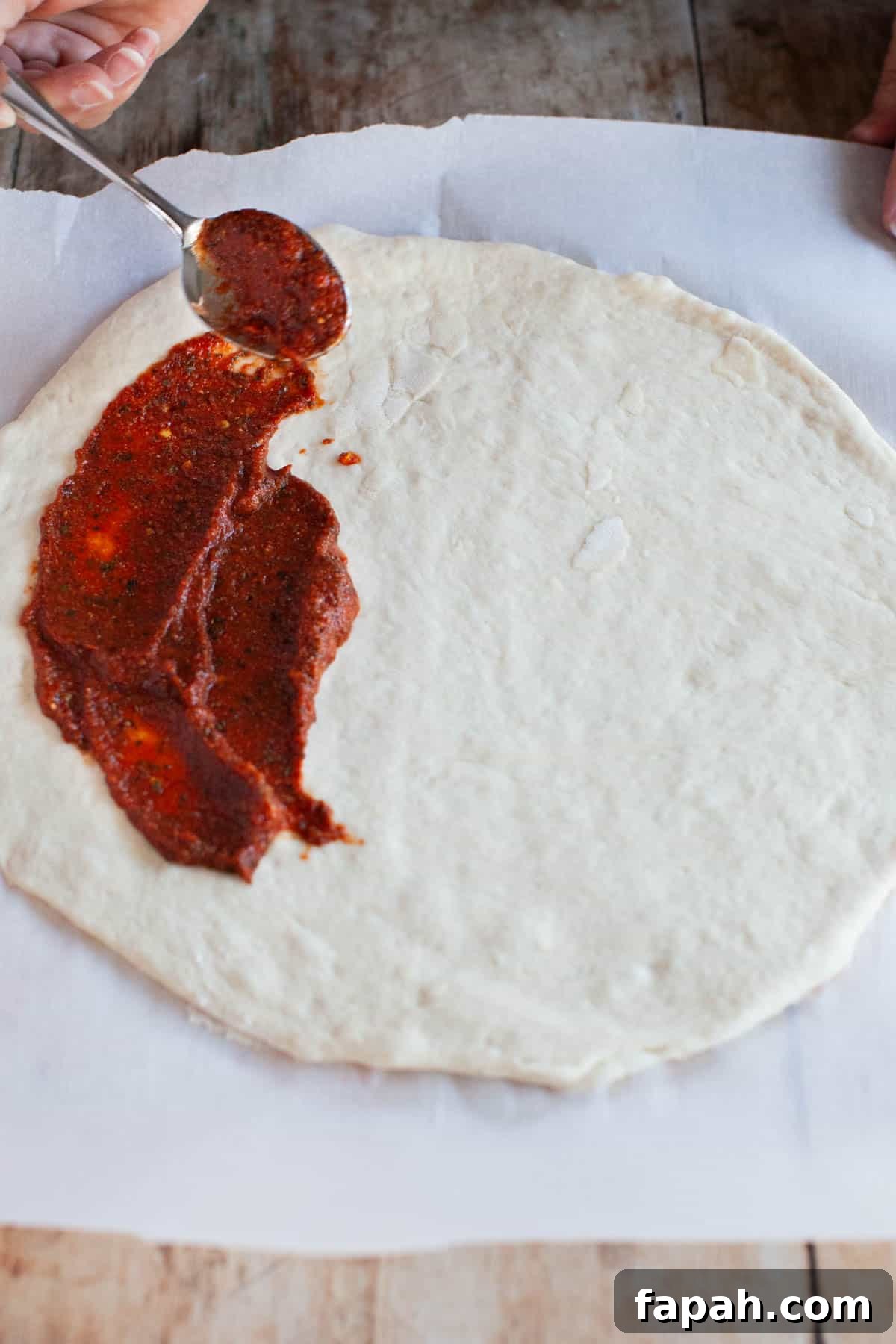 Homemade Pizza Sauce Recipe for Authentic, Restaurant-Quality Flavor 2 a spoon spreading pizza sauce on dough.