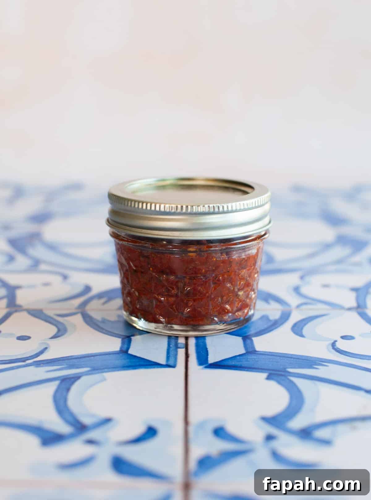 Homemade Pizza Sauce Recipe for Authentic, Restaurant-Quality Flavor 4 a small jar of pizza sauce with basil leaves on blue tiles.