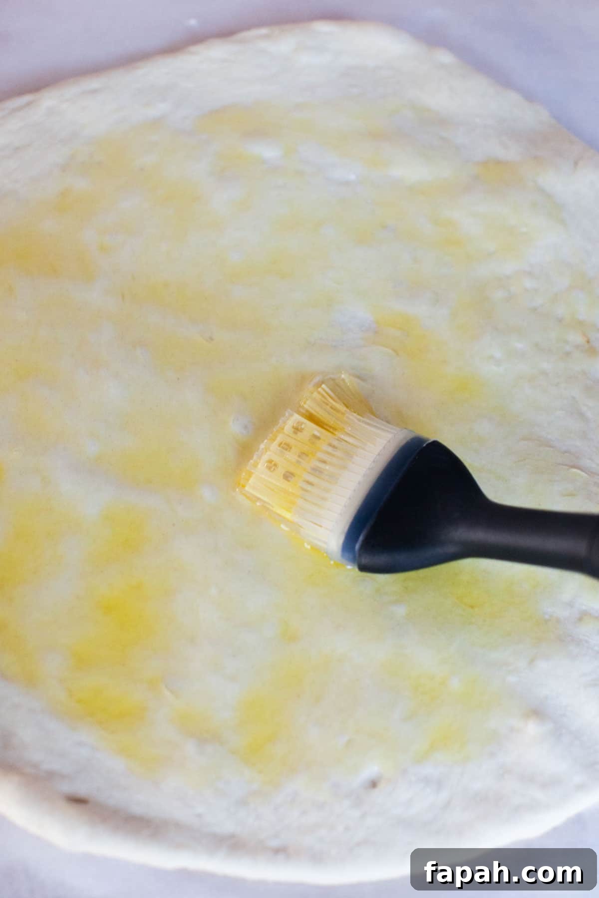 Homemade Pizza Sauce Recipe for Authentic, Restaurant-Quality Flavor 6 Olive oil being spread over a unbaked pizza dough with a basting brush.