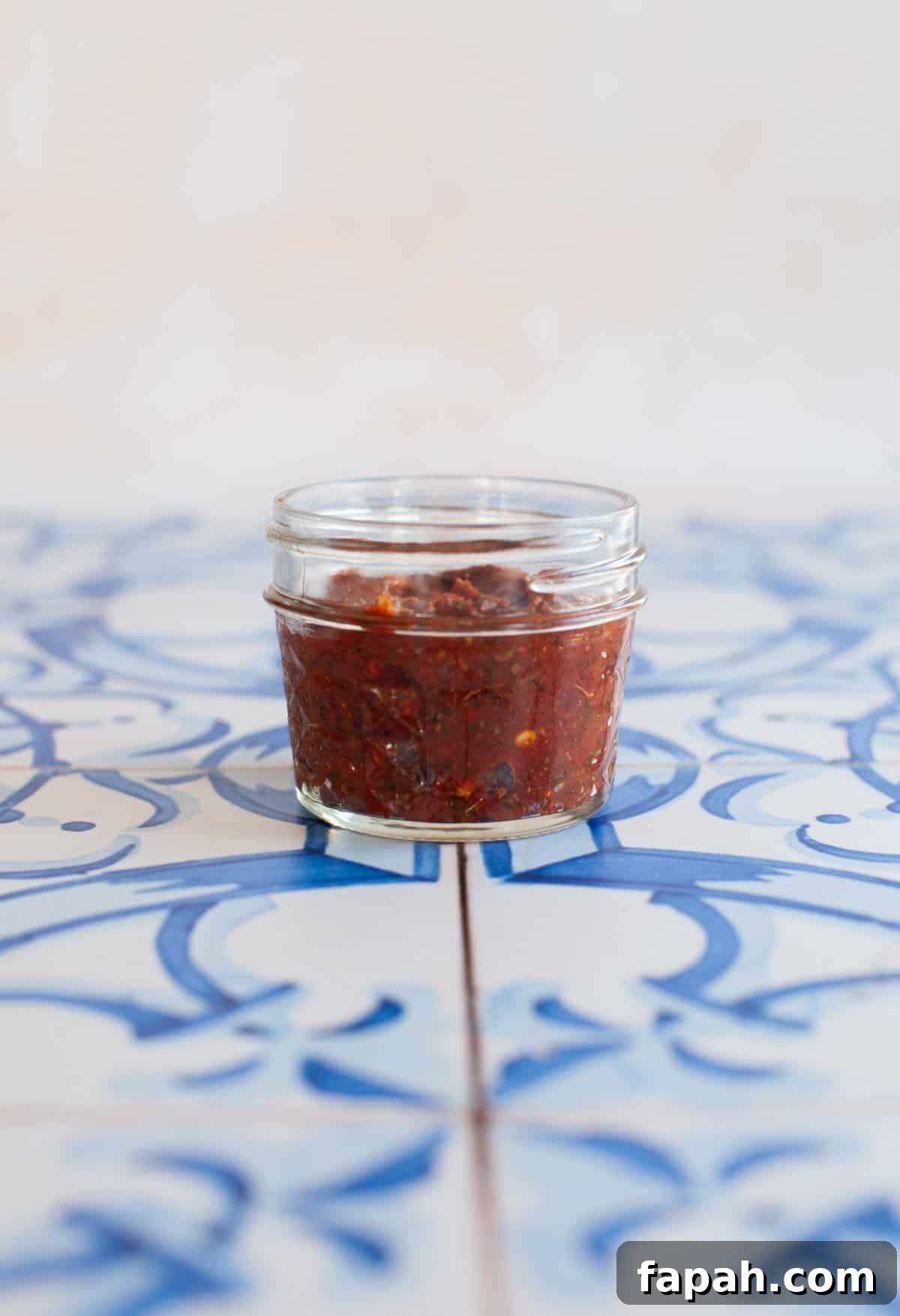 Homemade Pizza Sauce Recipe for Authentic, Restaurant-Quality Flavor 9 a small jar of pizza sauce with basil leaves on blue tiles.