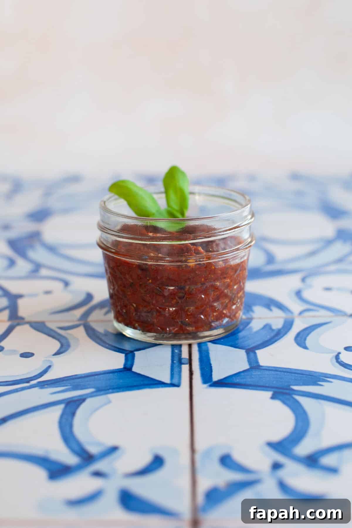 Homemade Pizza Sauce Recipe for Authentic, Restaurant-Quality Flavor 10 a small jar of pizza sauce with basil leaves on blue tiles.