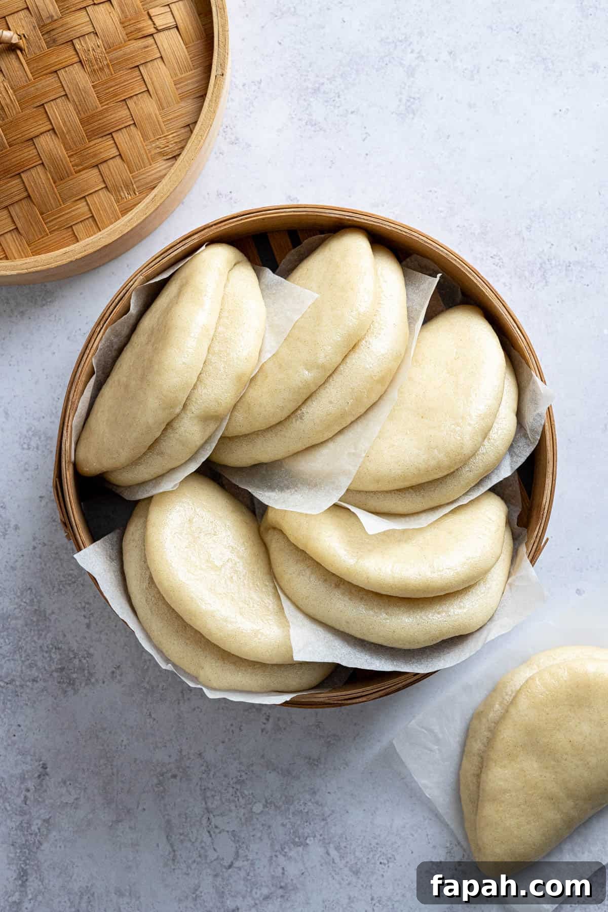 Bao buns on pieces of baking paper in a bamboo steamer.