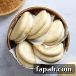 Bao buns on pieces of baking paper in a bamboo steamer.