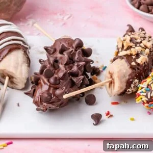 Four frozen chocolate covered banana halves on sticks are adorned with an assortment of toppings: nuts, chocolate chips, and vibrant sprinkles.