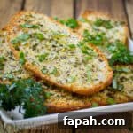 15 Creative Recipes for Using Leftover Bread 7 Side shot of multiple slices of garlic bread garnished with fresh herbs on a white plate.