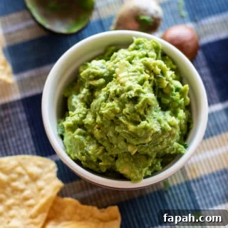 Creamy Homemade Guacamole Recipe for Parties and Everyday Meals 10 White bowl containing homemade guacamole, chips on table.