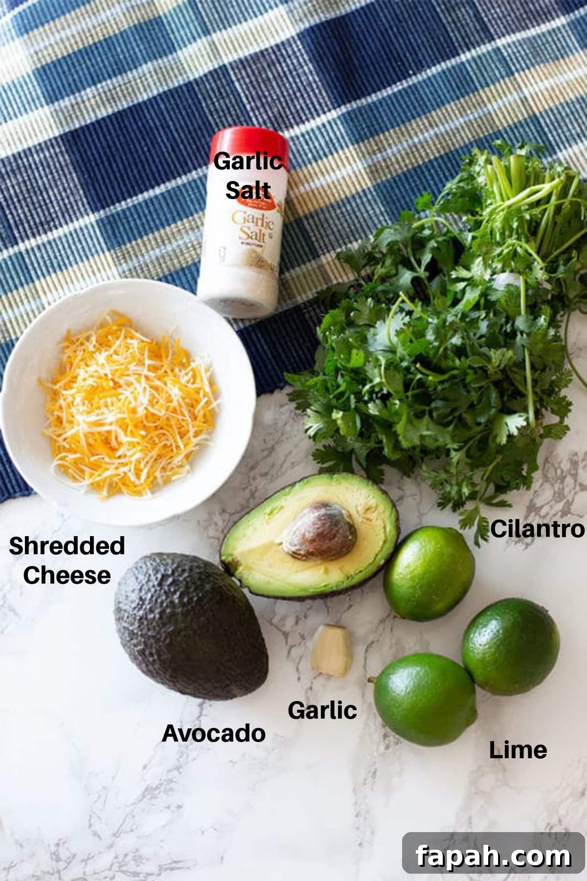 Creamy Homemade Guacamole Recipe for Parties and Everyday Meals 3 Cheese, garlic salt, cilantro, avocado, lime and garlic on a counter to make guacamole.