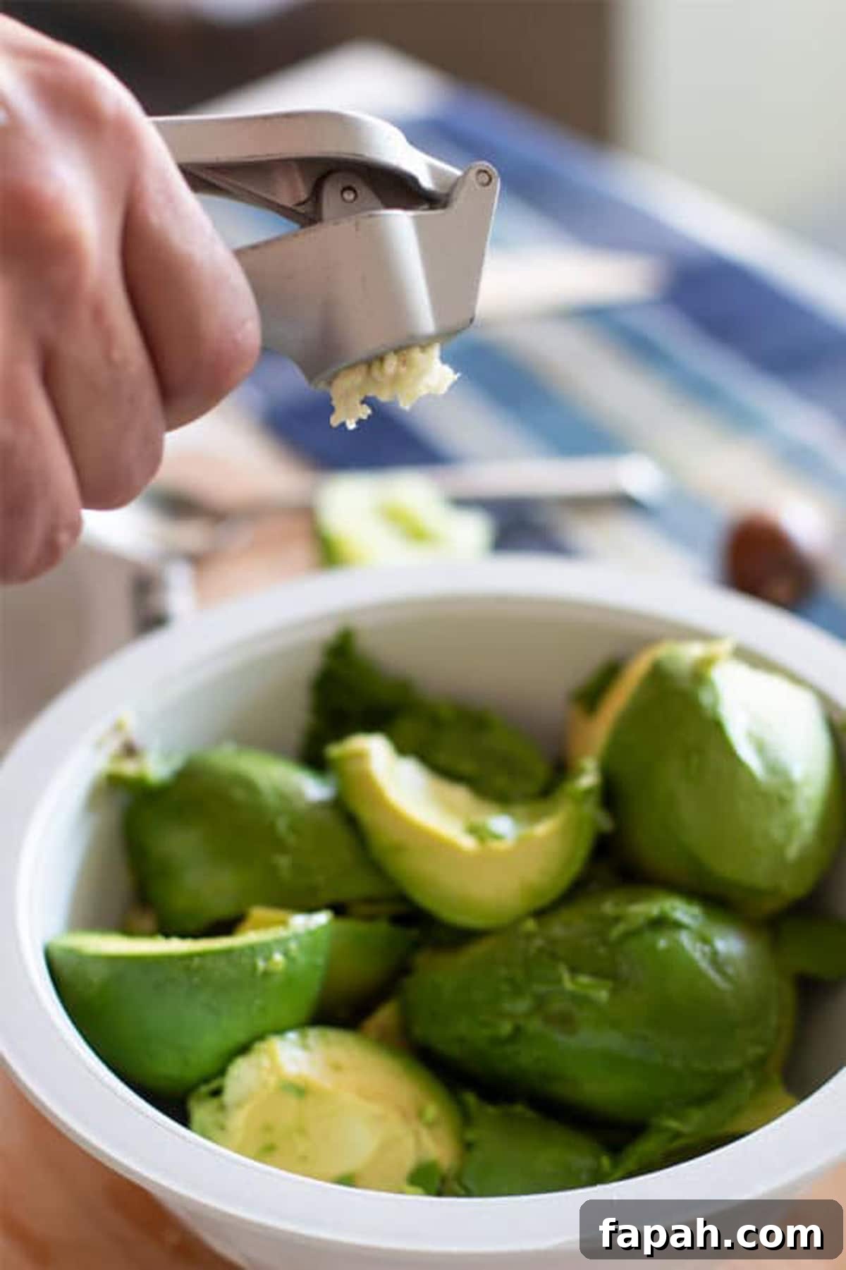 Creamy Homemade Guacamole Recipe for Parties and Everyday Meals 6 Pressing fresh garlic into the bowl of avocados.