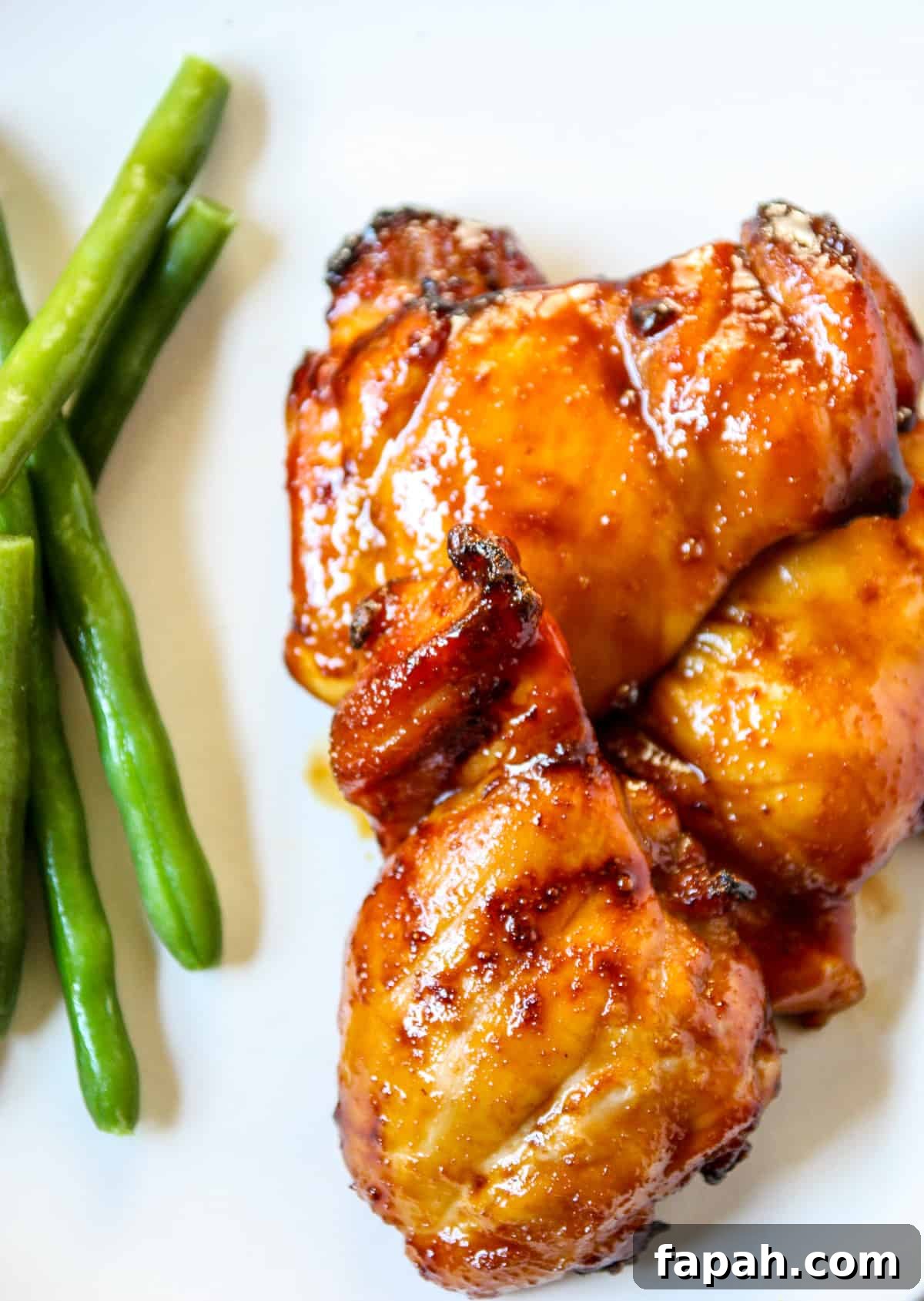 Teriyaki chicken alongside green beans on a white plate.