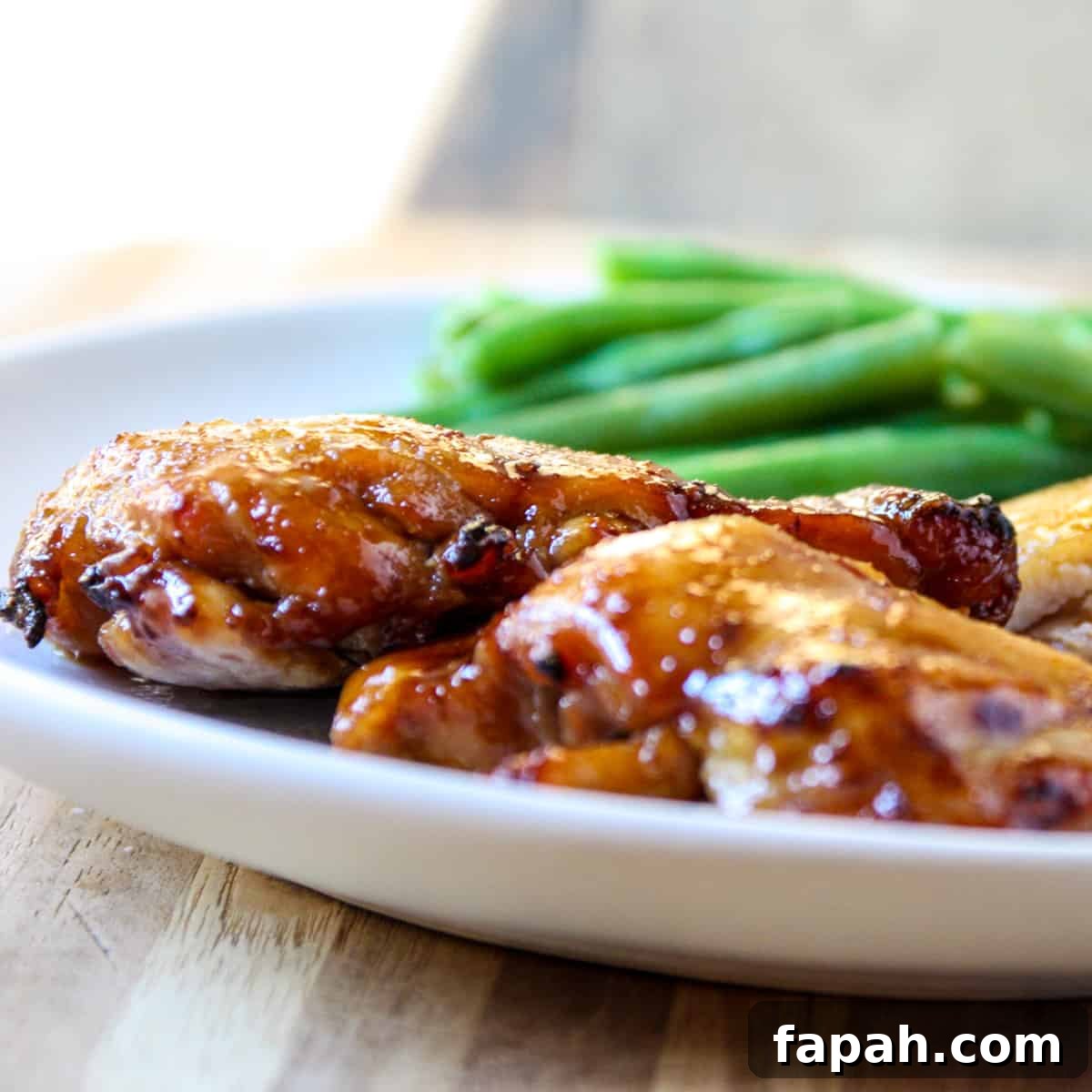A side view of the chicken on a plate with green beans blurred in the background.