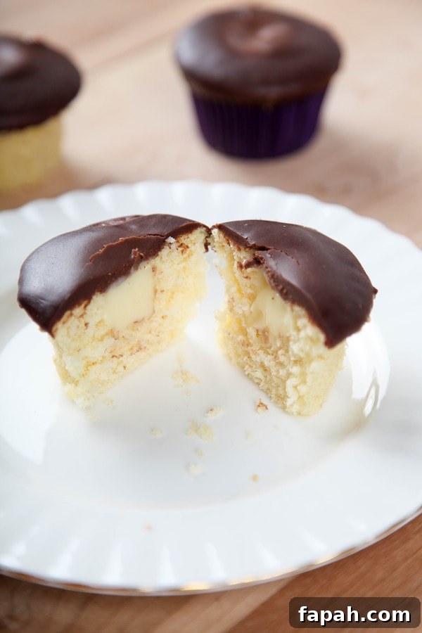 a cupcake topped with chocolate ganache cut in half to reveal a pastry cream center.