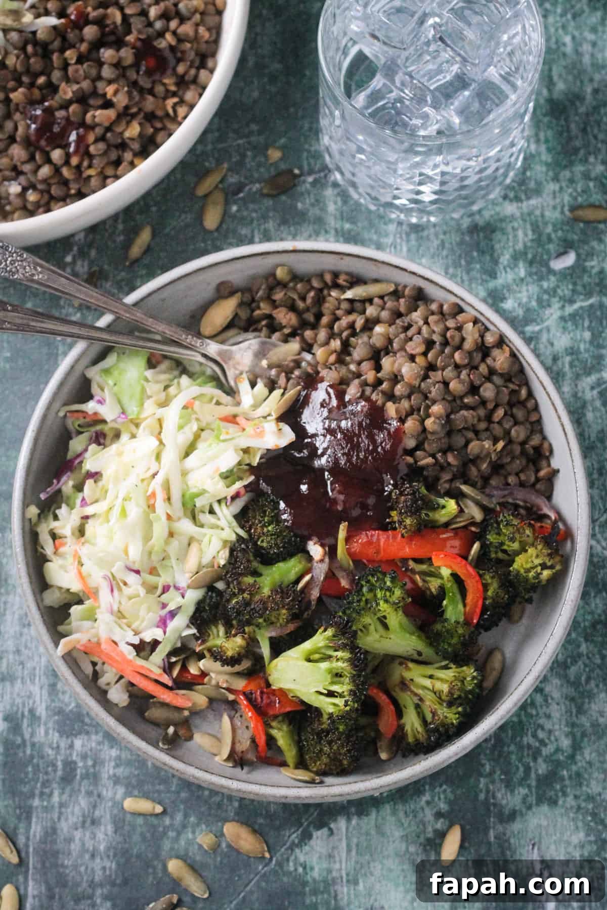 Two forks in a pile of lentils next to roasted broccoli, coleslaw, and bbq sauce.