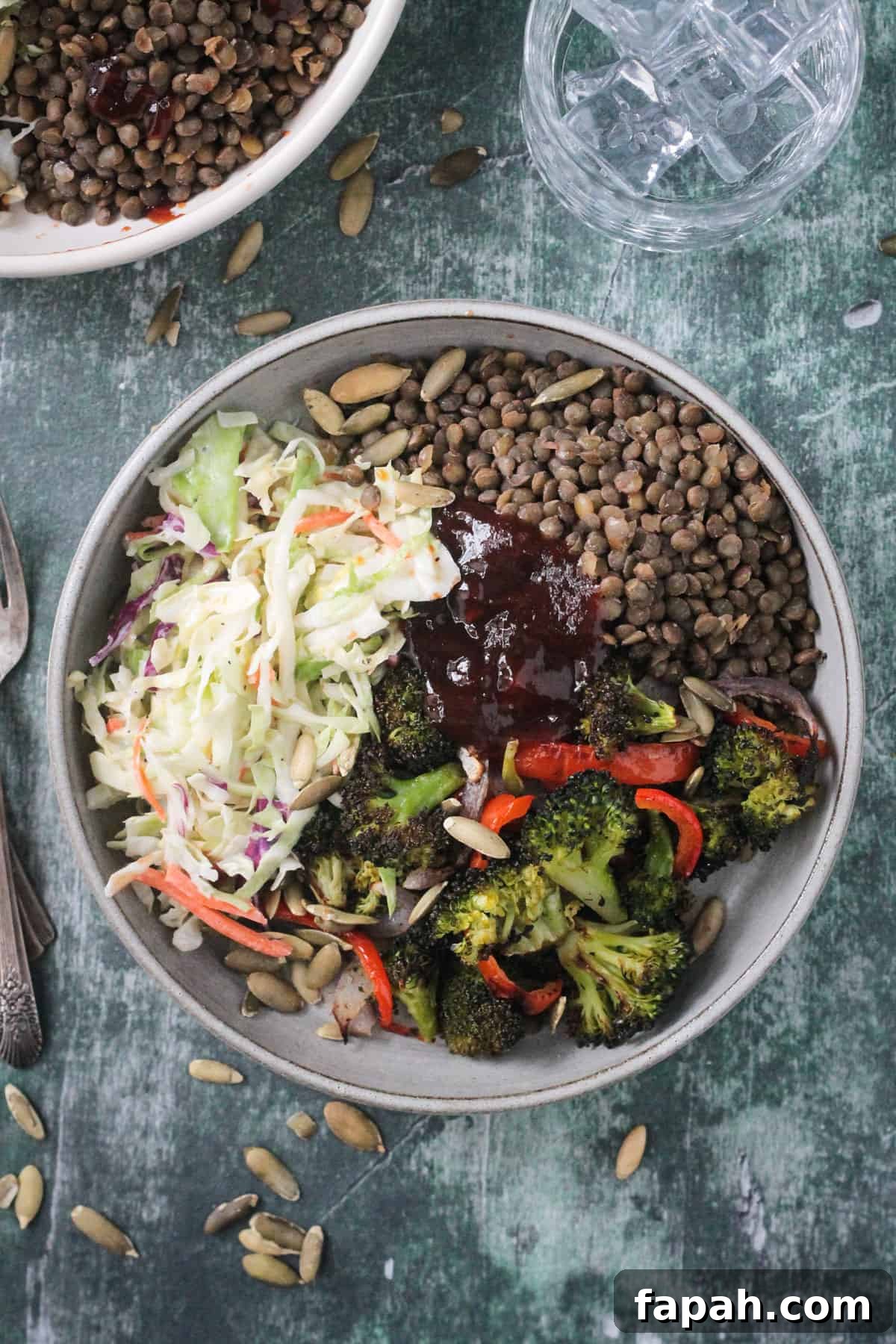 Lentils, coleslaw, roasted broccoli, and bbq sauce in a gray flat bowl.