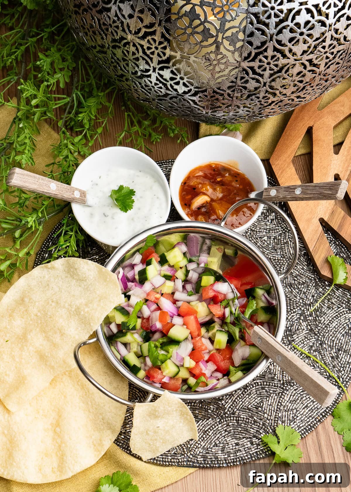 Indian Onion Salad with a spoon on top of the salad in a Balti dish with, mint raita, mango chutney and poppadoms served on the side.