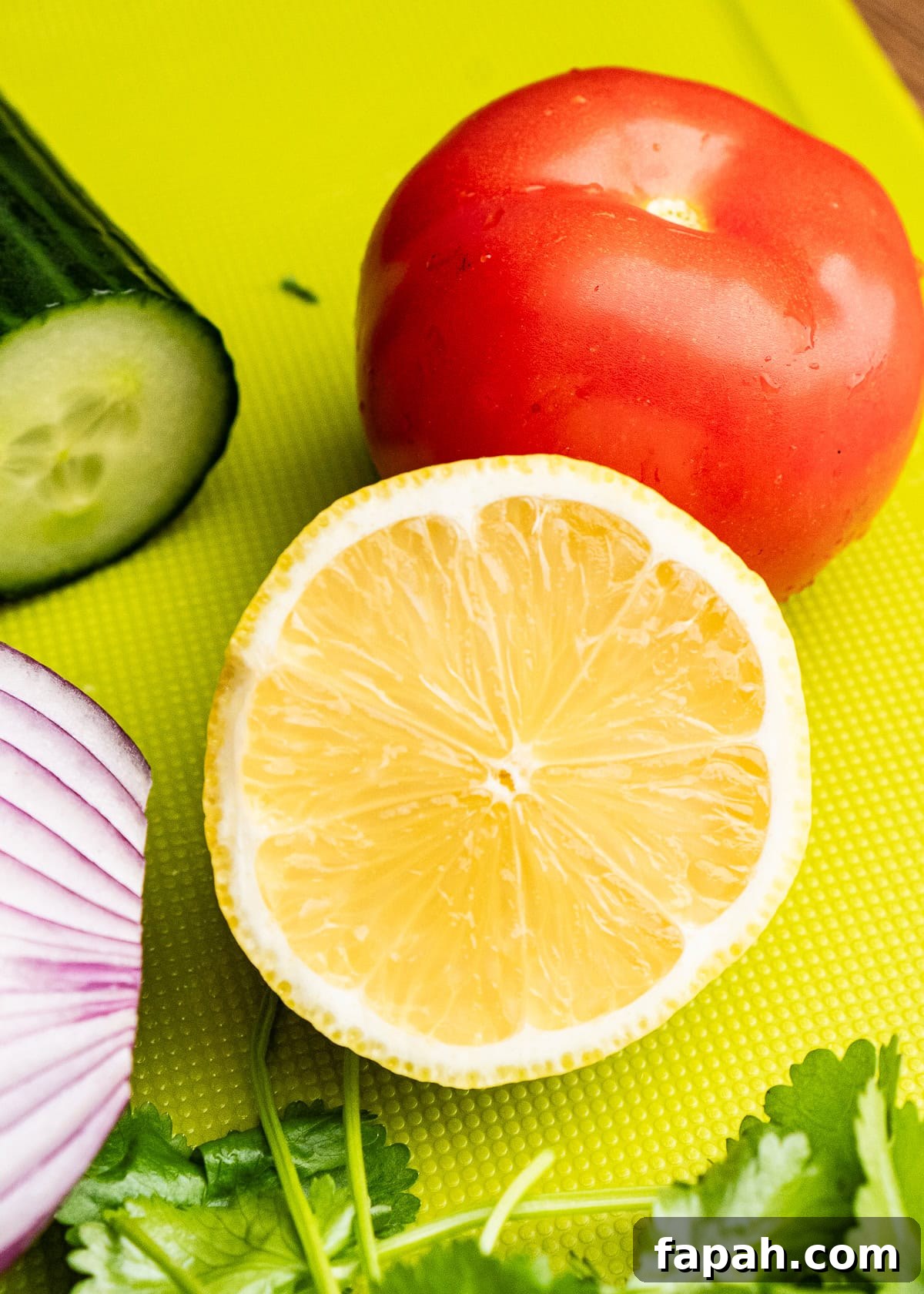 A cut half a lemon on a green chopping board with a tomato in the background