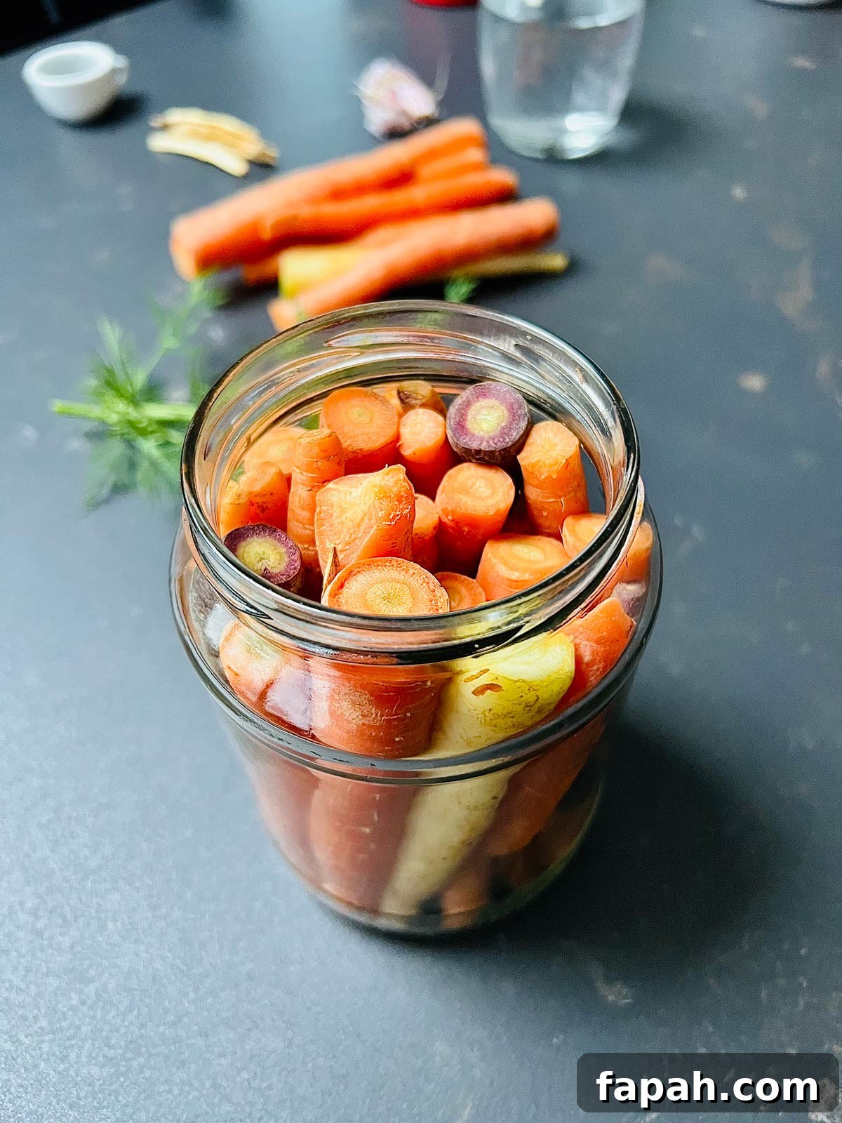 Birds eye view of carrots, being arranged in a jar ready for pickling.