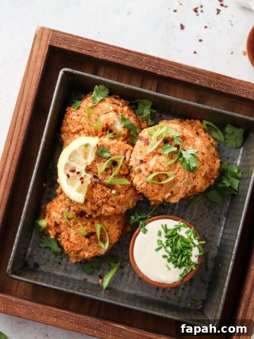 Whole30 crab cakes on a black plate with aioli dipping sauce, green herb garnish and a lemon wedge