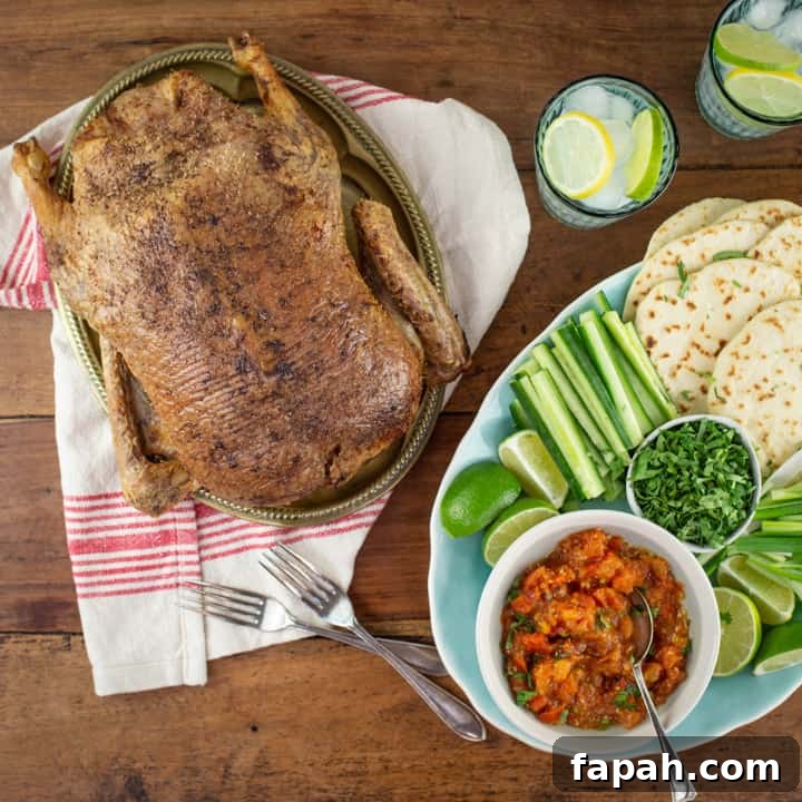 wooden table with pale blue platter of homemade soft taco shells, cucumber, limes and a whole crispy roast duck