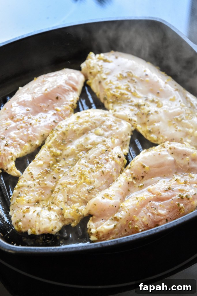 cooking marinated chicken in a cast iron grill pan for the greek chicken salad meal prep bowls.