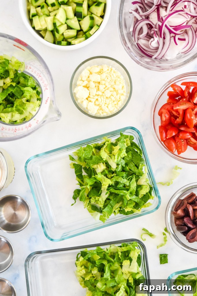 adding romaine and assembling greek chicken salad meal prep in glass containers.