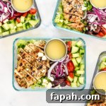 greek chicken salad meal prep bowls with dressing in glass container.
