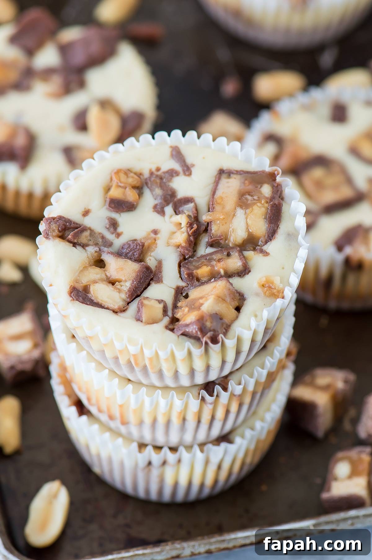 Mini Snickers Cheesecakes: Bite-Sized Candy Bar Desserts 3 mini snicker’s cheesecakes stacked 3 high on a dark metal baking sheet