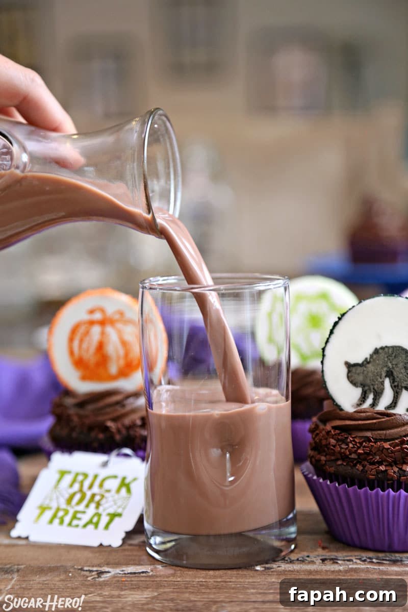 Stamped Halloween Cupcakes - pouring chocolate milk into a glass with chocolate cupcakes nearby | From SugarHero.com
