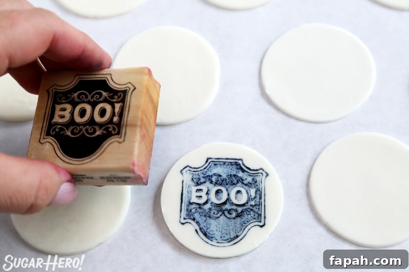 Stamped Halloween Cupcakes - stamping a fondant circle with a "Boo!" stamp | From SugarHero.com