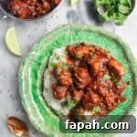 Chicken rogan josh on a bed of white rice on a green plate, with more curry in a small silver dish on the side.