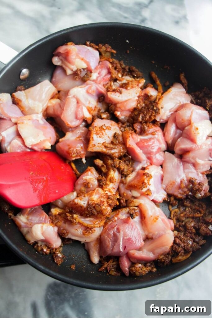 Diced chicken in a small frying pan with spices through it.