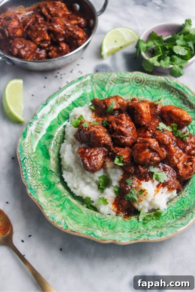 Close up of chicken rogan josh on rice on a small green plate with more curry in the background.