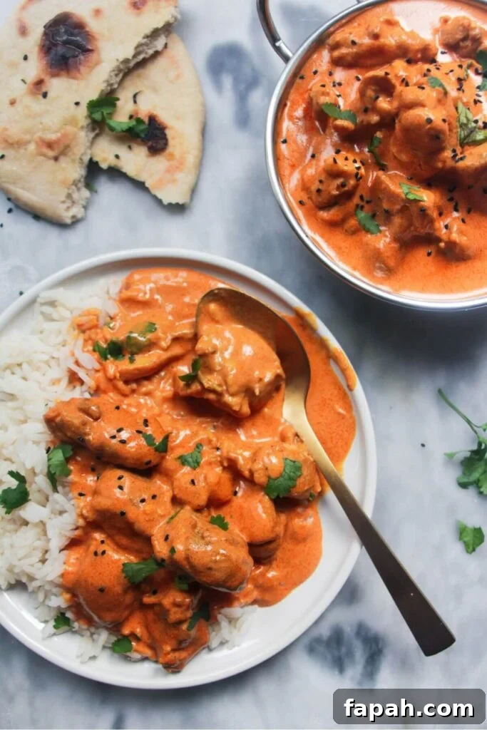 White plate with rice and butter chicken with bowl of butter chicken in the background and garlic naan.