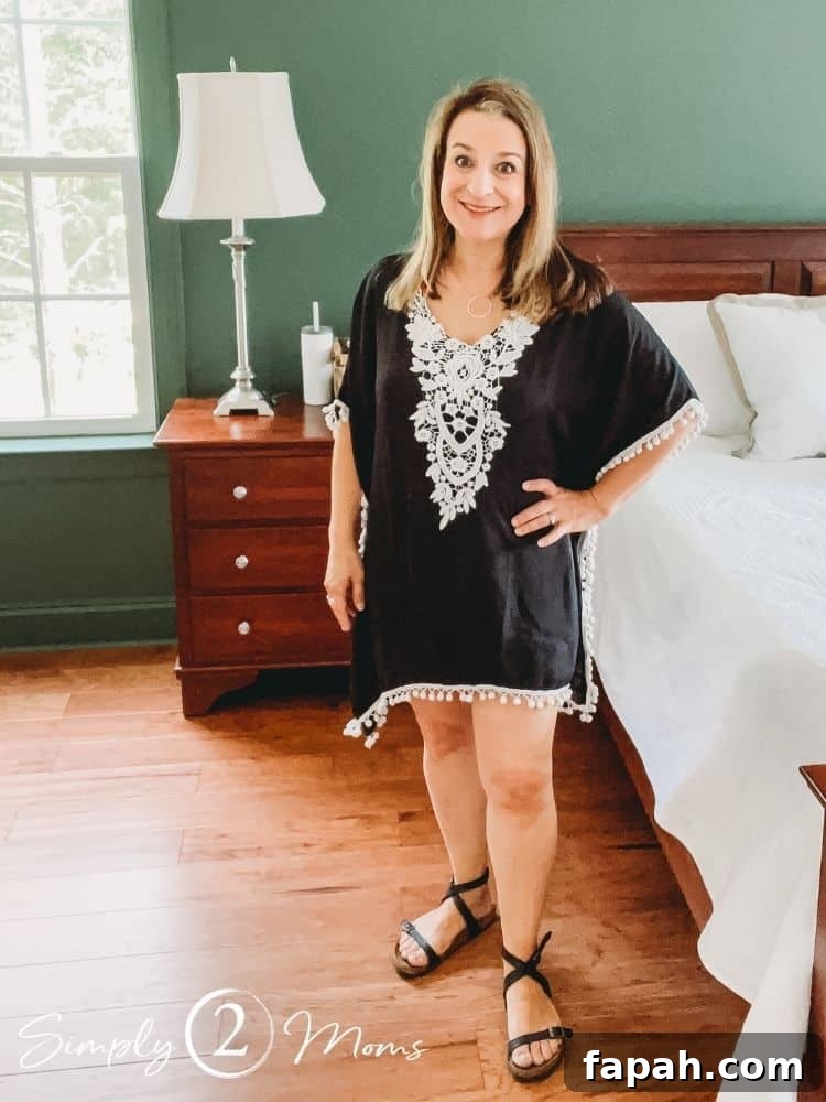 Woman wearing a black coverup dress with white lace detail in the front and white pompom fringe along the bottom