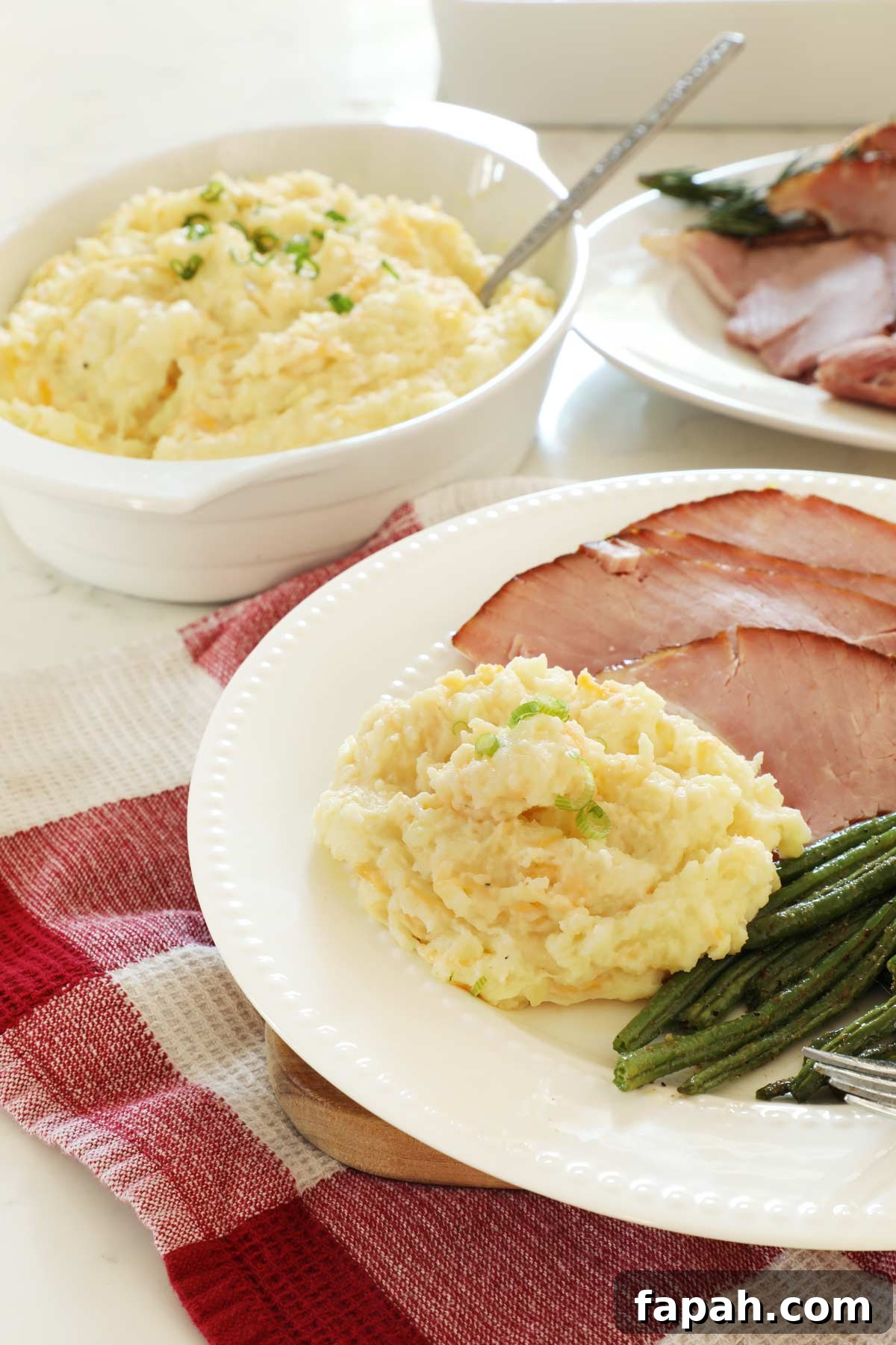 A white plate with cheesy mashed potatoes, ham and green beans.