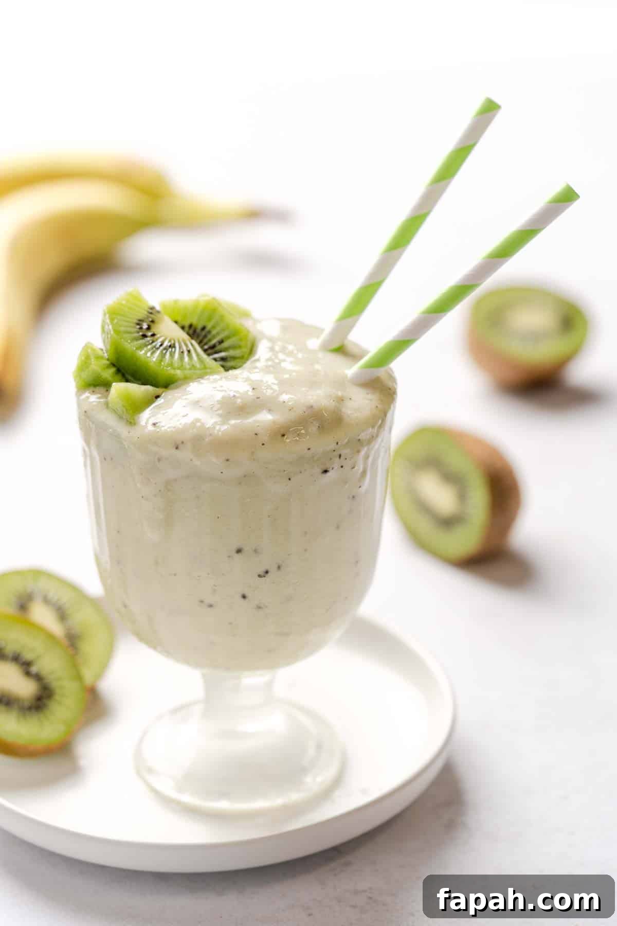 smoothie in glass with kiwi on top and two straws