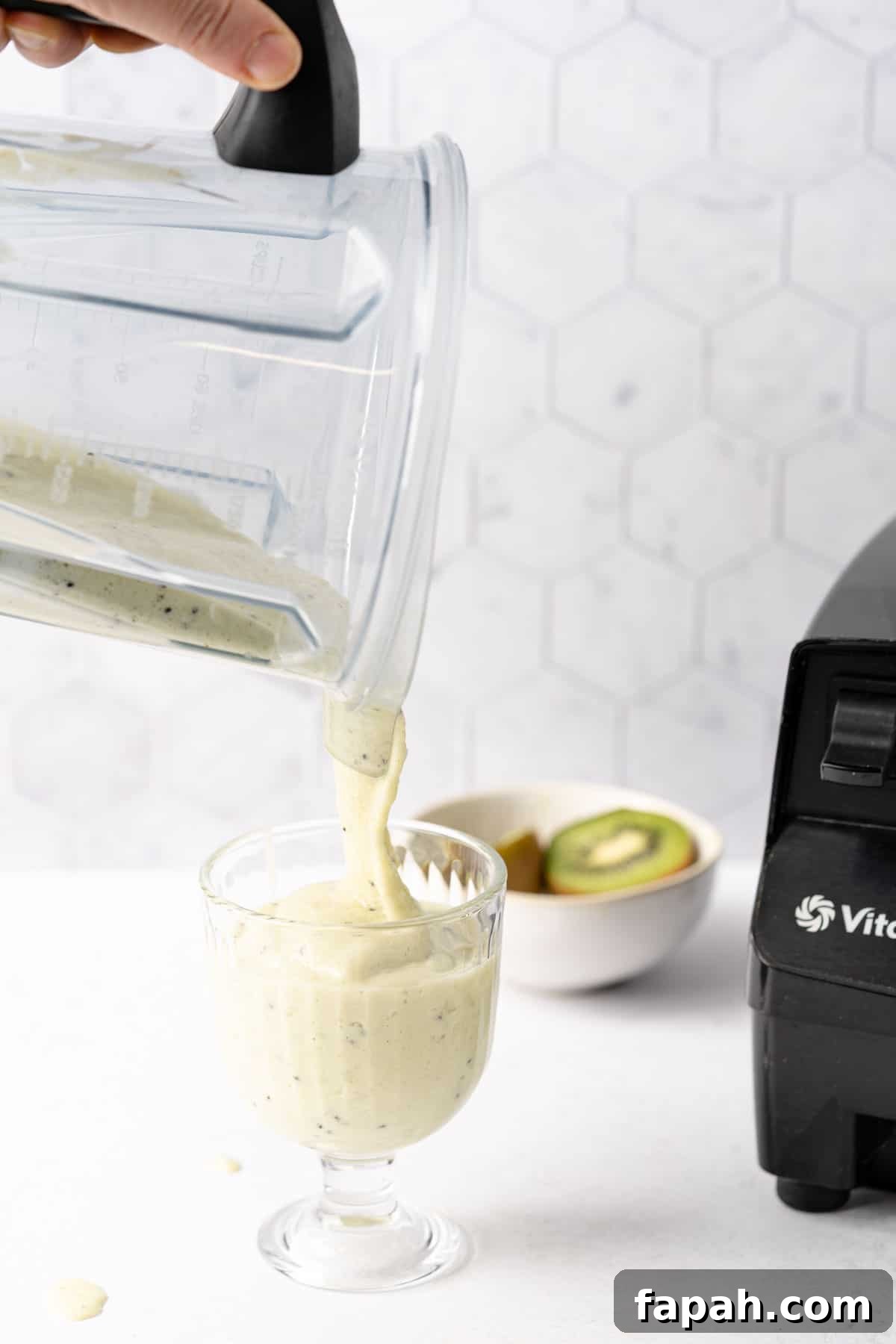 hand holding blender pitcher pouring smoothie into glass
